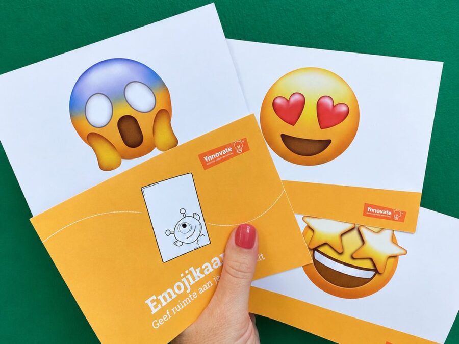 Pakket Emojikaarten van Ynnovate in de hand, met twee kaarten op een groene achtergrond