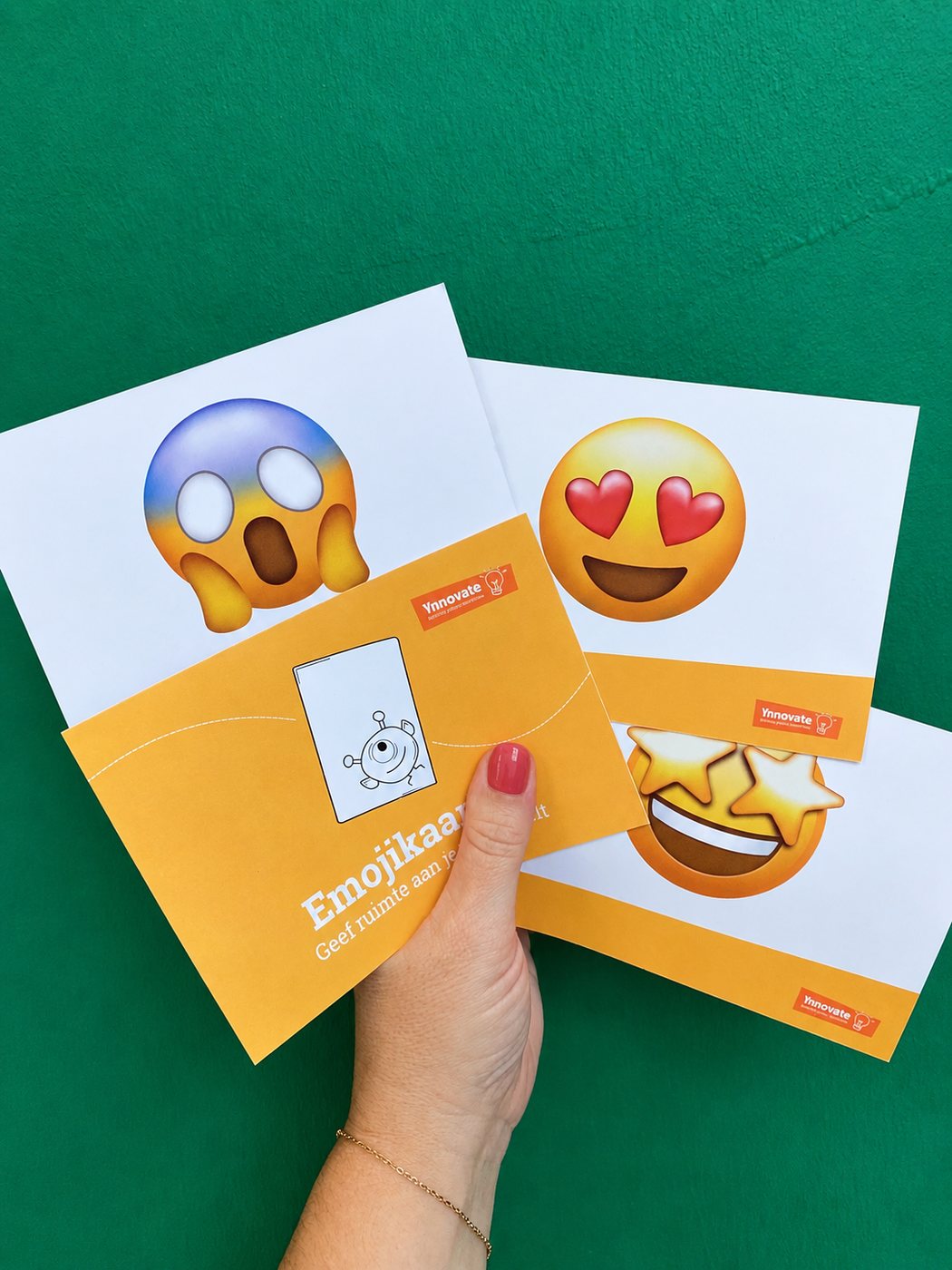 Pakket Emojikaarten van Ynnovate in de hand, met twee kaarten op een groene achtergrond