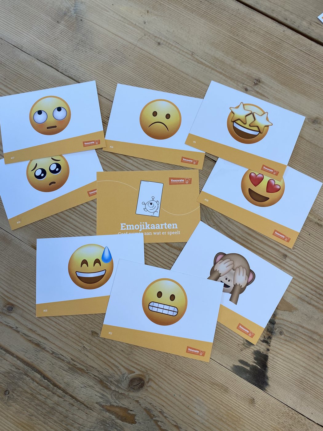 Emojikaarten van Ynnovate uitgelegd op een houten vloer, met het pakket in het midden